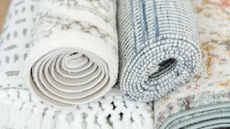 Close-up of four rolled patterned rugs on a wooden floor featuring fringes and varied textures