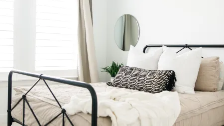 Minimalist bedroom with black metal bed frame, neutral bedding, patterned pillow, and modern ceiling light.