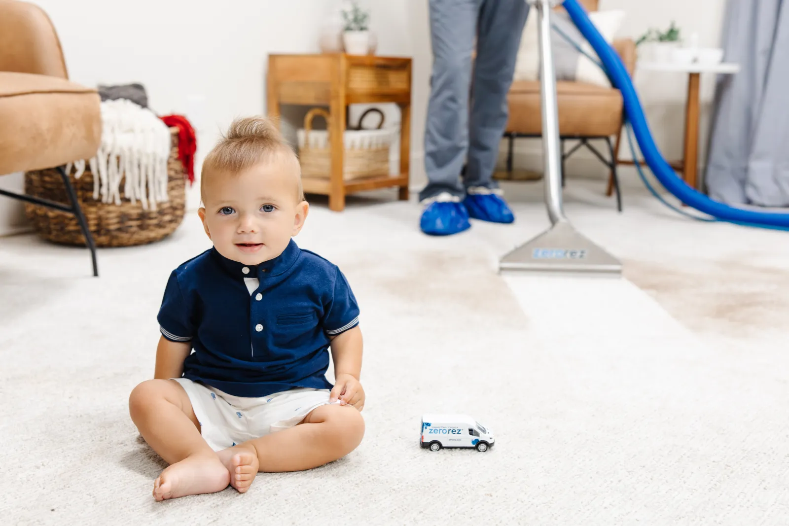 a baby on the floor with a toy car and cleaning wand