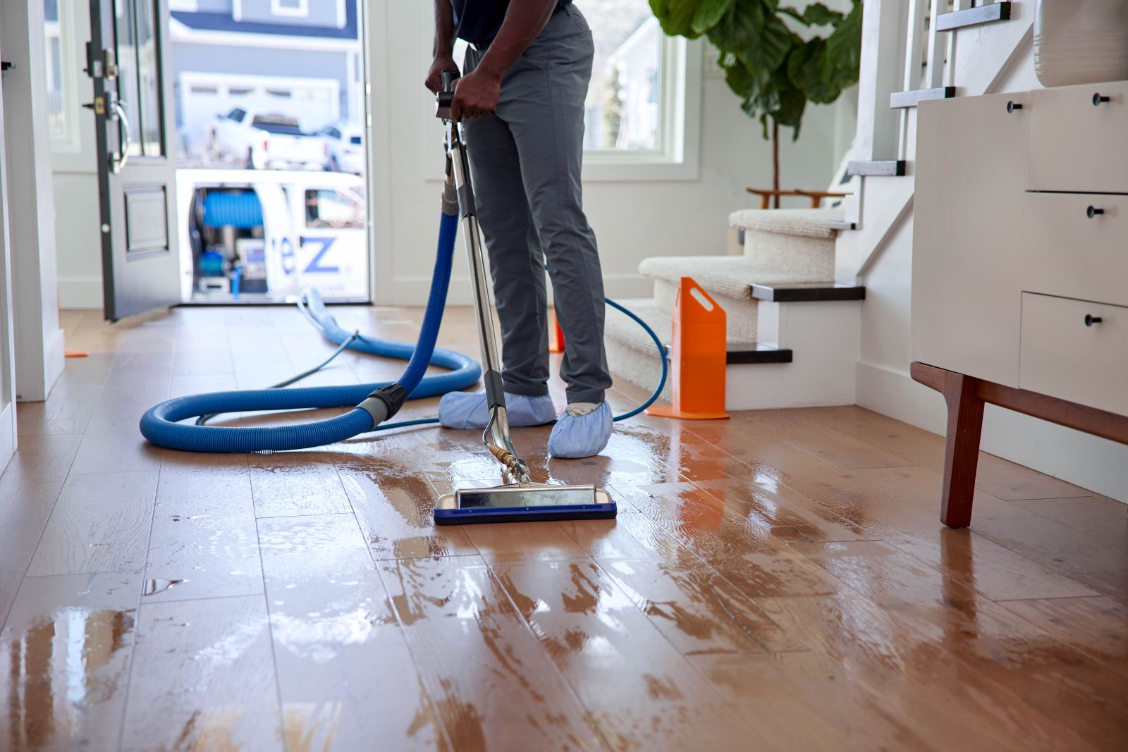 one reason why hardwood floors are slippery is because they are wet. Zerorez&reg; technician is seen cleaning a hardwood floor in a home with the door open behind him and the Zerorez van parked outside