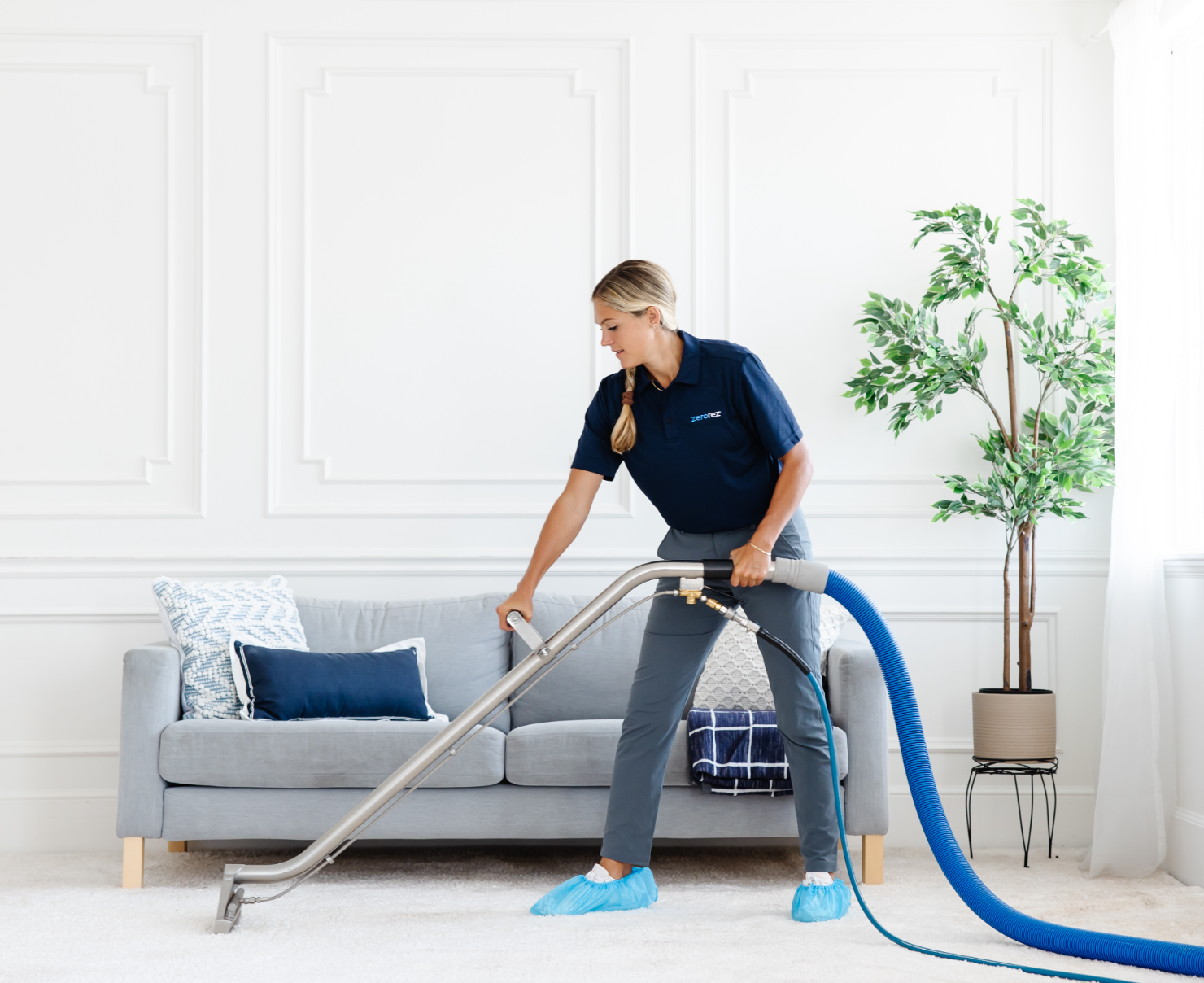 Zerorez female technician cleaning a living room with a Zr&trade; Wand, which extracts dirt and grime from a white carpet, leaving no sticky residue behind after cleaning